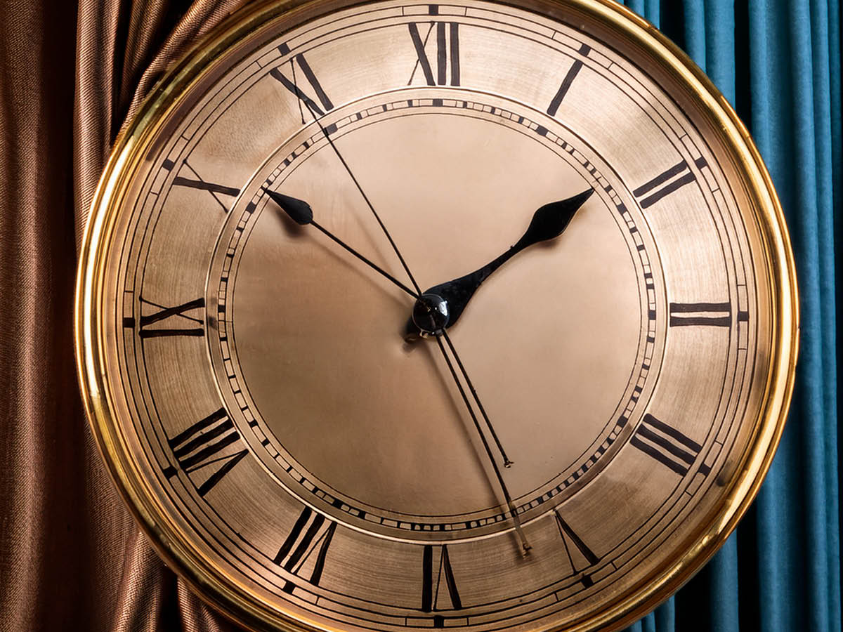 Eine nostalgische große goldene Uhr. Im Hintergrund schwere Vorhänge.